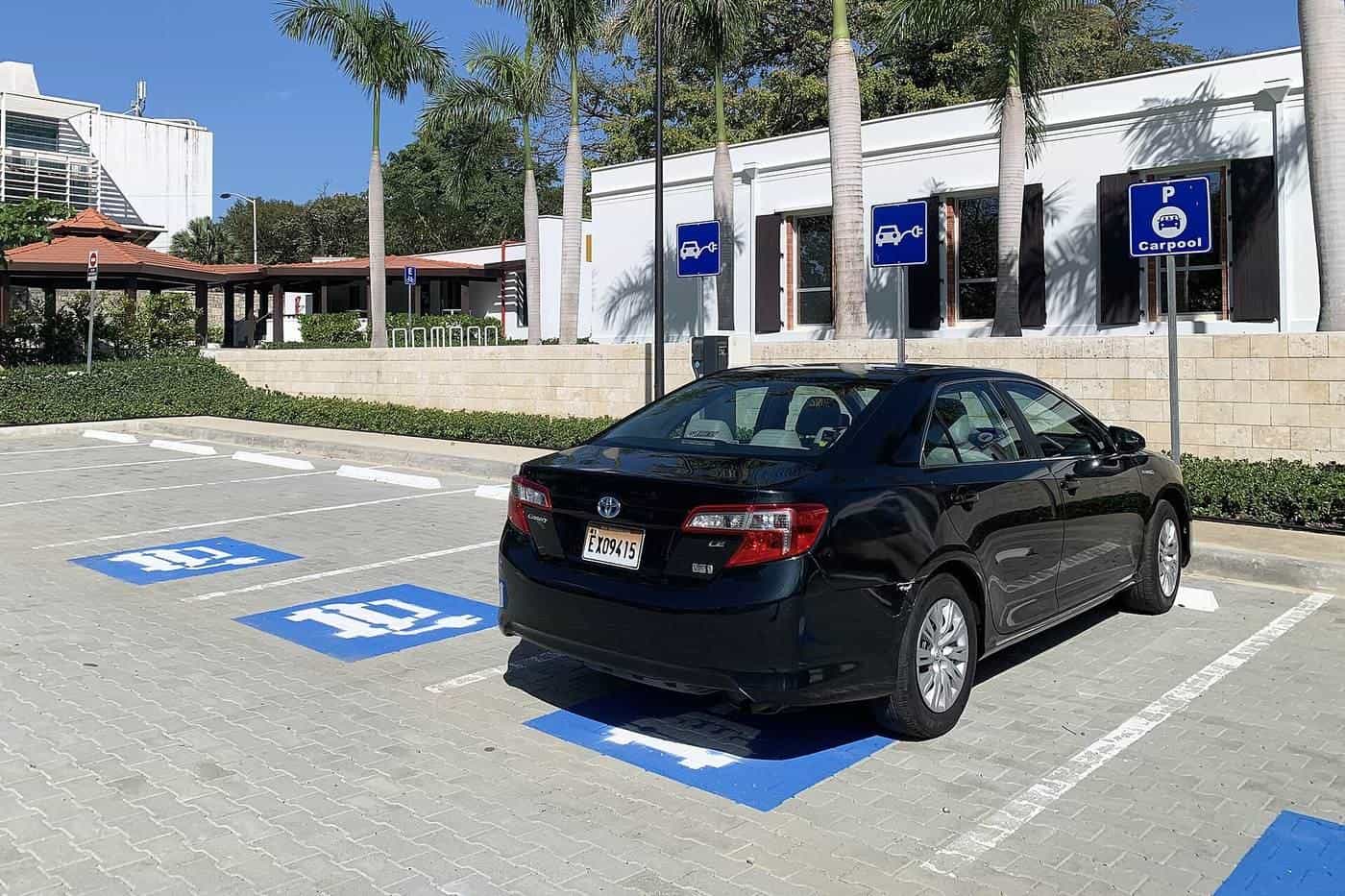 A black hybrid sedan parked in a marked bay outside a building on a sunny day