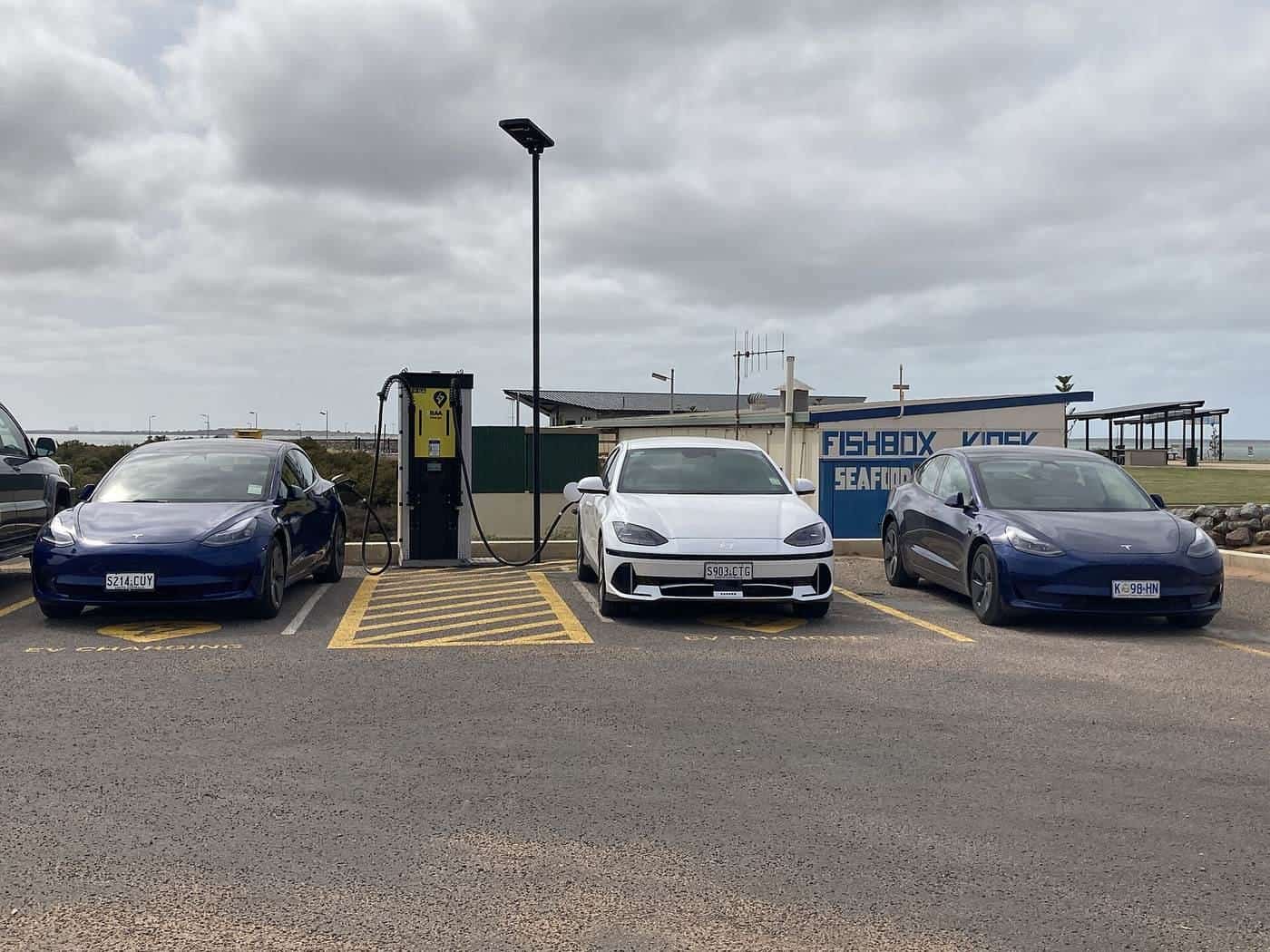 Several electric cars parked at a roadside charging station under a cloudy sky in regional South Australia