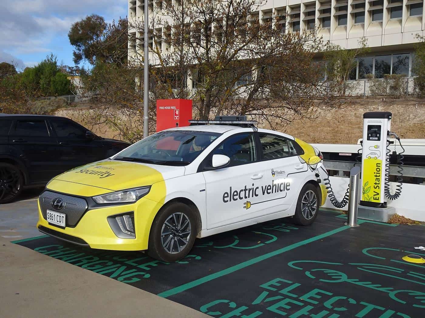 A yellow and white electric car plugged into a charging post on a painted charging bay