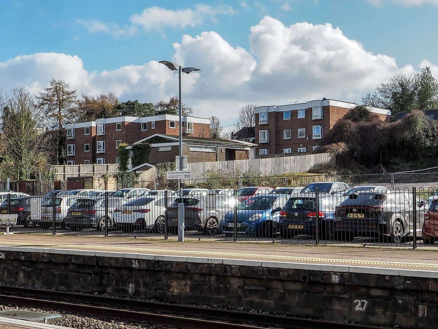 A car park filled with cars in front of brick apartment buildings under a blue sky