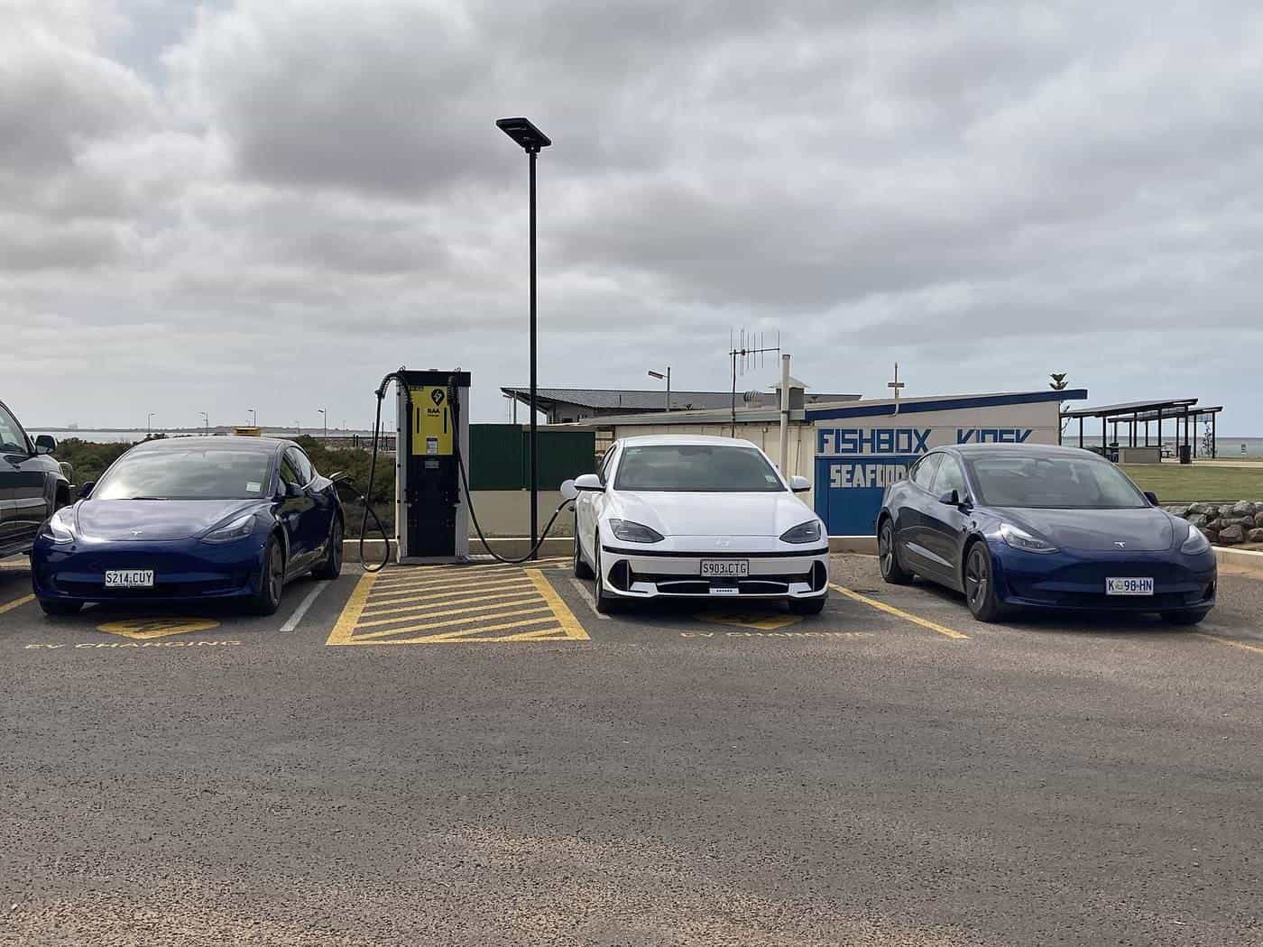 Several electric cars parked at a roadside charging station under a cloudy sky in regional South Australia