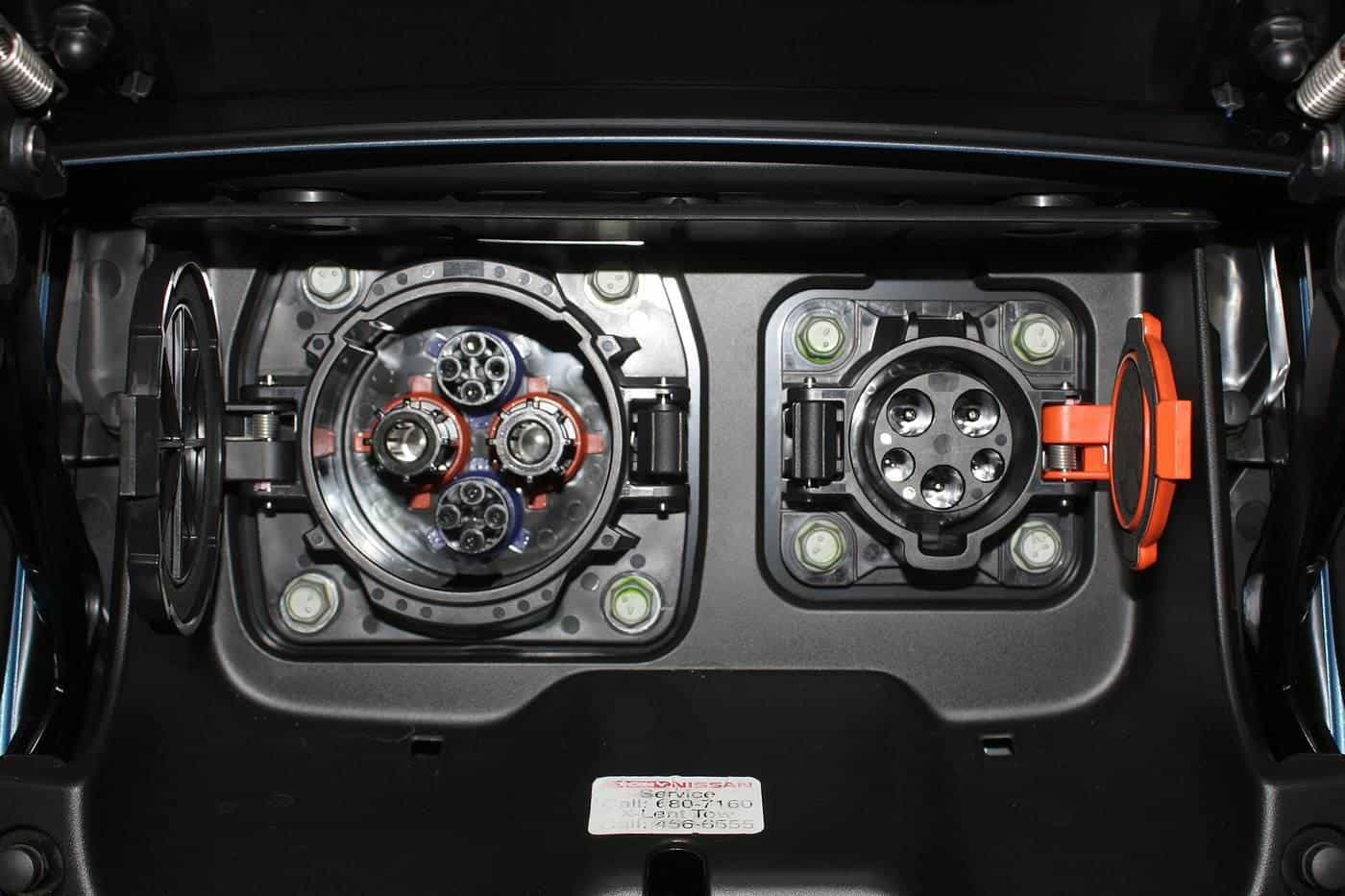 The open charging port flap of an electric car showing an AC socket and a DC fast-charging socket side by side