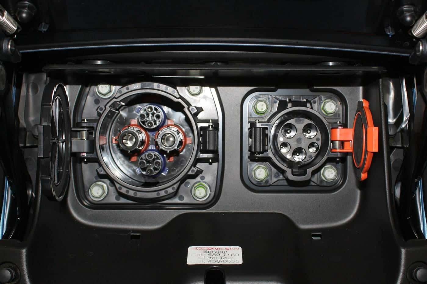 The open charging port flap of an electric car showing an AC socket and a DC fast-charging socket side by side