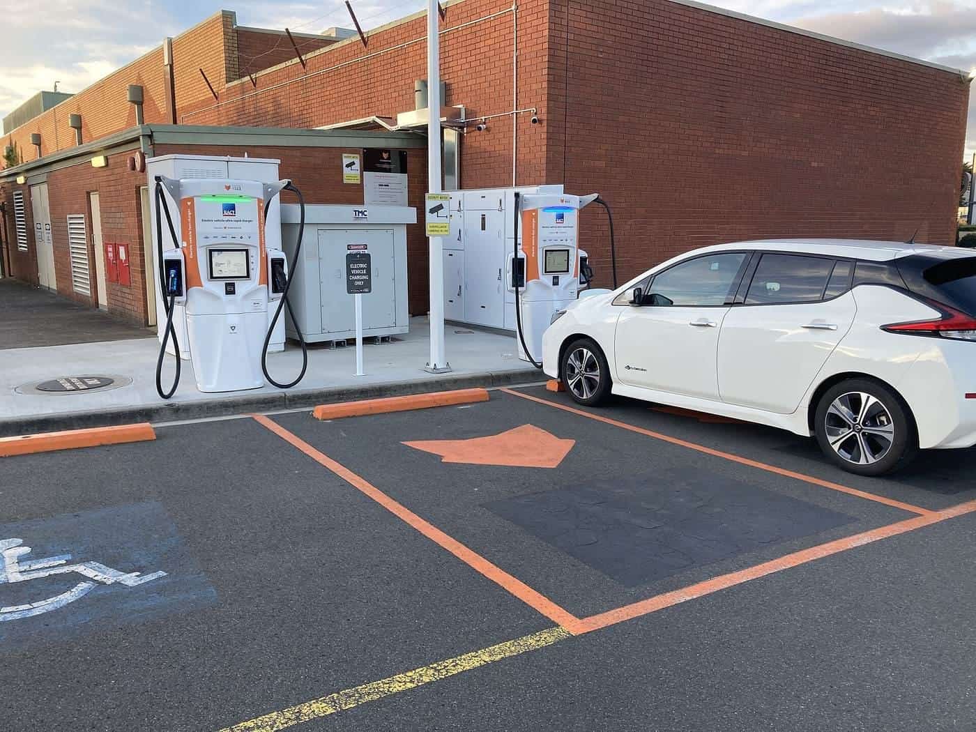 A white electric hatchback parked at a two-bay fast-charging station with orange markings in Kings Meadows, Tasmania