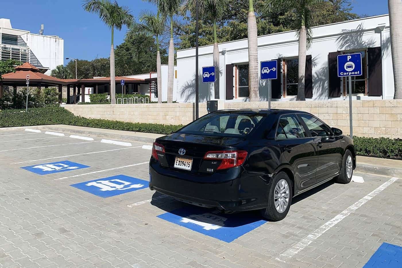 A black hybrid sedan parked in a marked bay outside a building on a sunny day