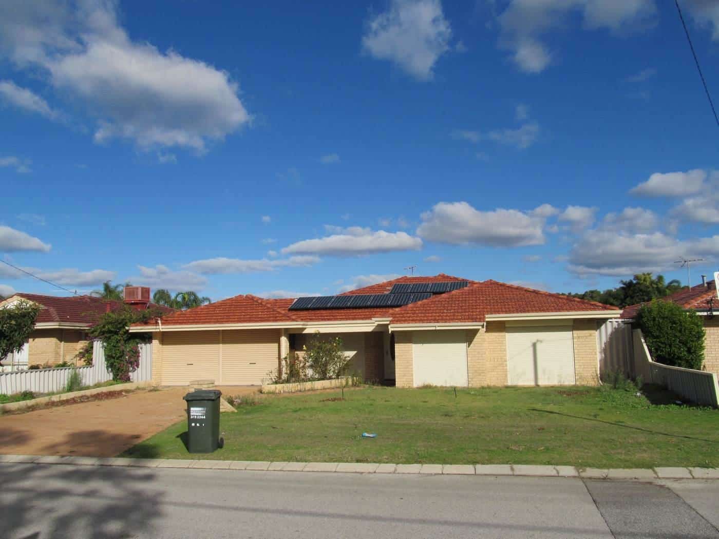 A brick suburban house with solar panels on its tiled roof under a blue sky with scattered clouds